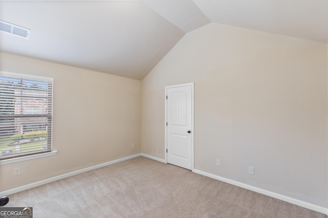 spare room featuring light carpet, visible vents, baseboards, and vaulted ceiling