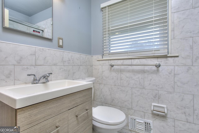 half bath with tile walls, visible vents, toilet, and vanity