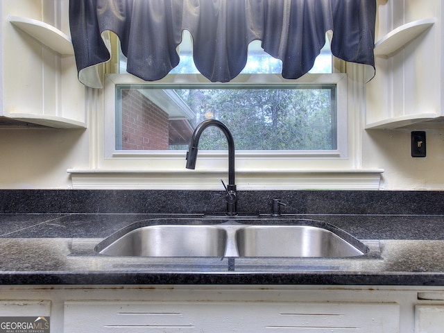 interior details featuring white cabinets, a sink, and dark stone counters