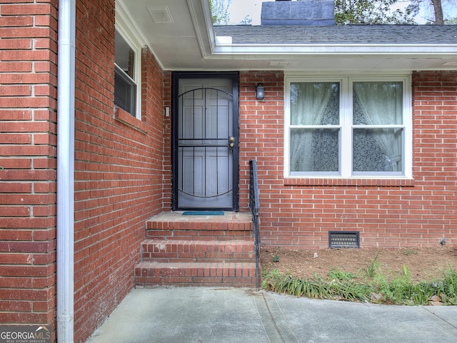 property entrance featuring crawl space, a chimney, a shingled roof, and brick siding