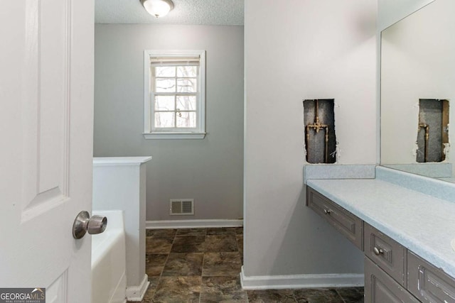 full bathroom featuring vanity, baseboards, a textured ceiling, a bathtub, and visible vents