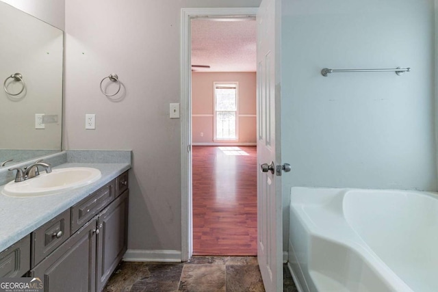 bathroom with baseboards, a tub, a textured ceiling, and vanity