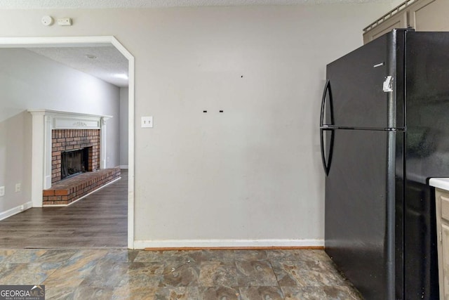 kitchen with freestanding refrigerator, baseboards, a fireplace, and a textured ceiling