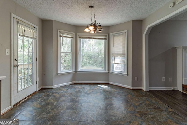 unfurnished dining area featuring baseboards, a textured ceiling, and an inviting chandelier