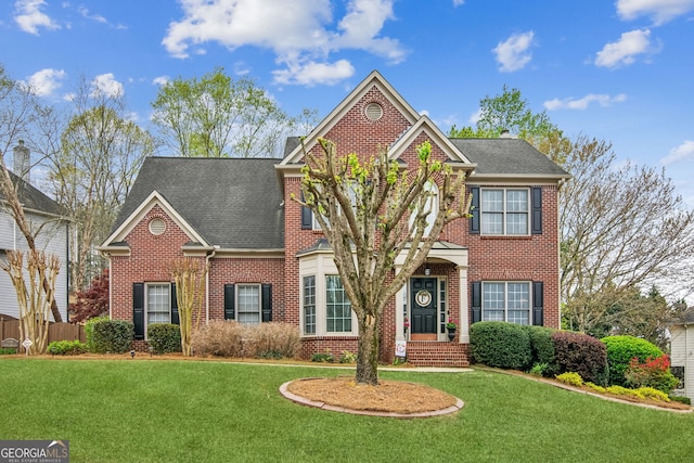 colonial-style house with brick siding, a front yard, a shingled roof, and fence