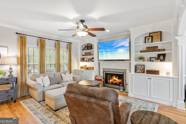 living room with a lit fireplace, light wood-style floors, ornamental molding, and a ceiling fan