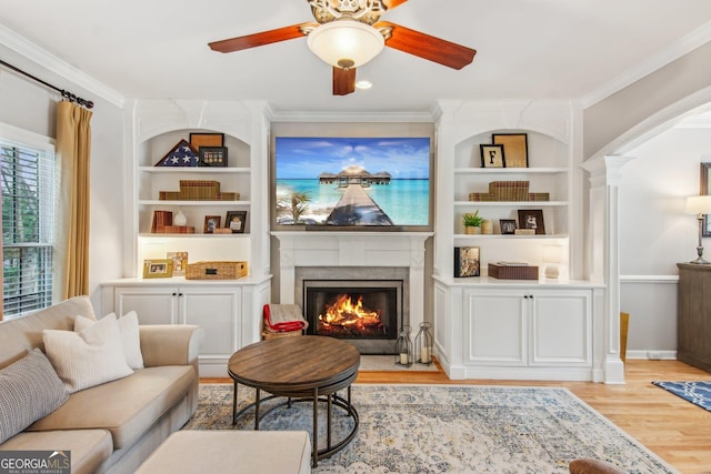 living area with a lit fireplace, crown molding, light wood-style floors, and ceiling fan