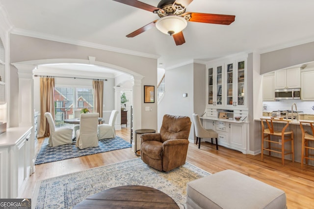 living area with arched walkways, a ceiling fan, light wood-style floors, and decorative columns
