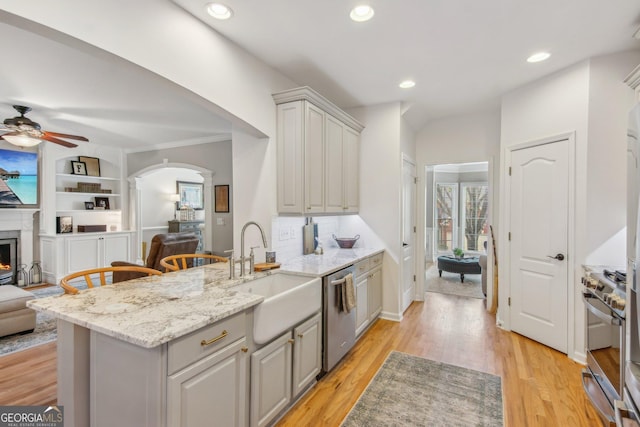 kitchen featuring open floor plan, stainless steel appliances, arched walkways, ceiling fan, and light wood-style flooring
