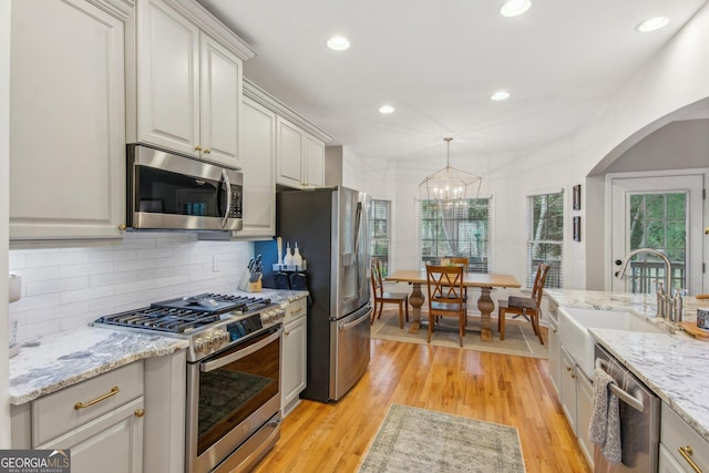 kitchen with light wood-style floors, a sink, stainless steel appliances, arched walkways, and an inviting chandelier