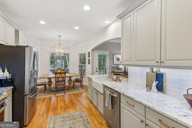 kitchen featuring light wood-style floors, a sink, tasteful backsplash, stainless steel appliances, and arched walkways