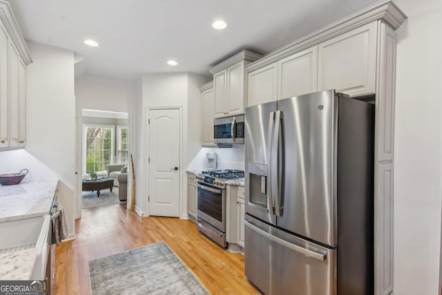 kitchen with light stone countertops, recessed lighting, tasteful backsplash, appliances with stainless steel finishes, and light wood-type flooring