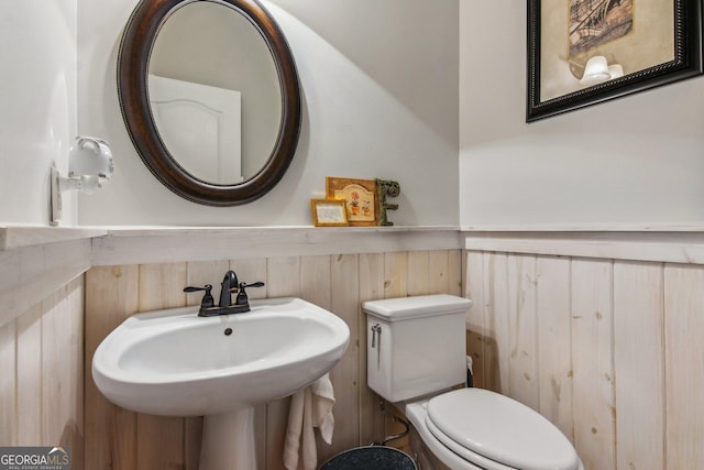 half bathroom with toilet, a sink, and wainscoting