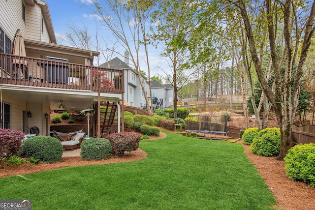 view of yard with a trampoline, fence, stairs, and a deck