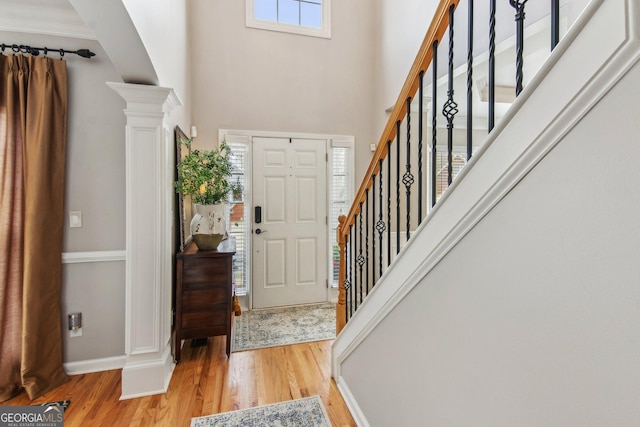 entrance foyer with ornate columns, stairs, baseboards, light wood-style floors, and a high ceiling