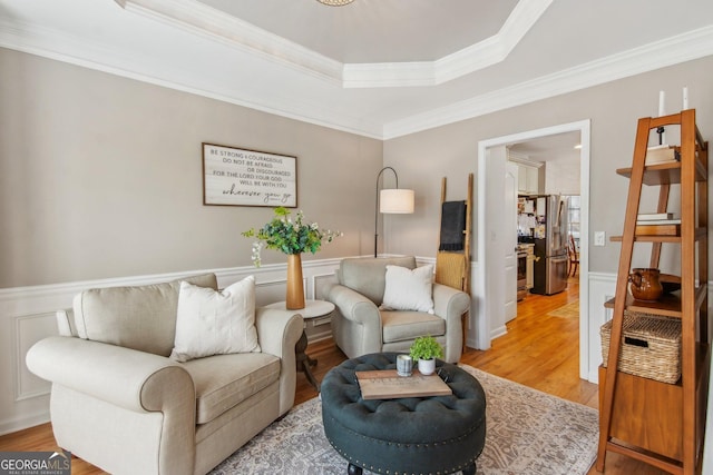 living room with a raised ceiling, ornamental molding, light wood-style floors, and wainscoting