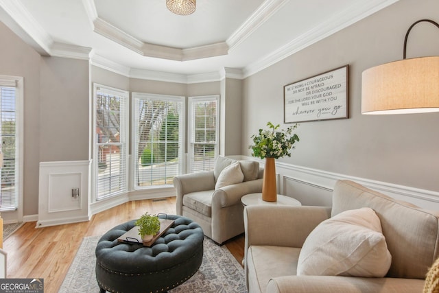 sitting room with a tray ceiling, crown molding, light wood-style floors, and wainscoting