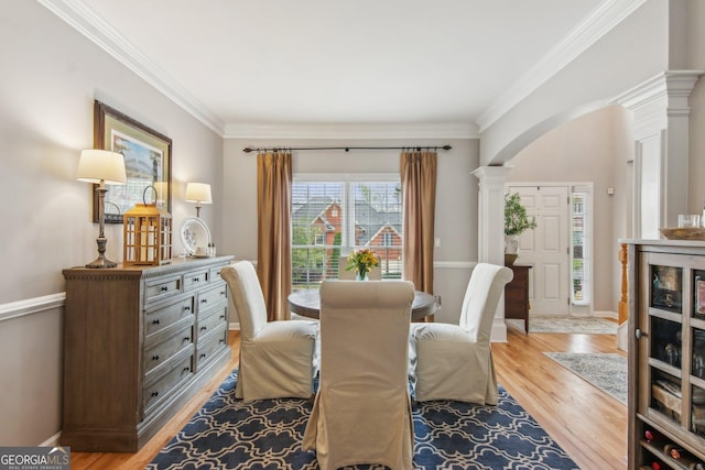 dining space with light wood-style floors, baseboards, arched walkways, ornamental molding, and ornate columns