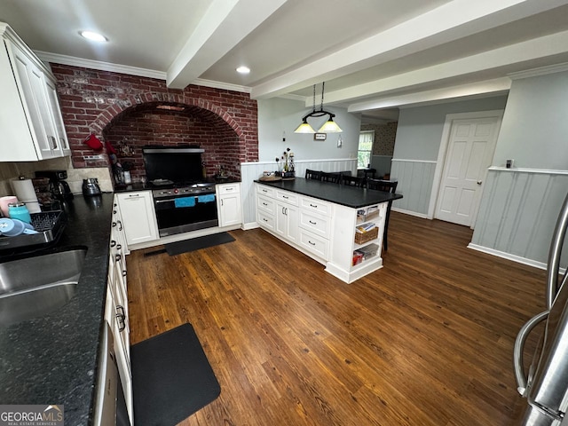 kitchen featuring a sink, dark countertops, a peninsula, wall oven, and a wainscoted wall