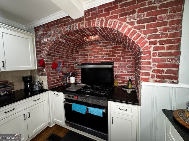 kitchen featuring white cabinets, dark wood-style flooring, dark countertops, brick wall, and range with gas cooktop