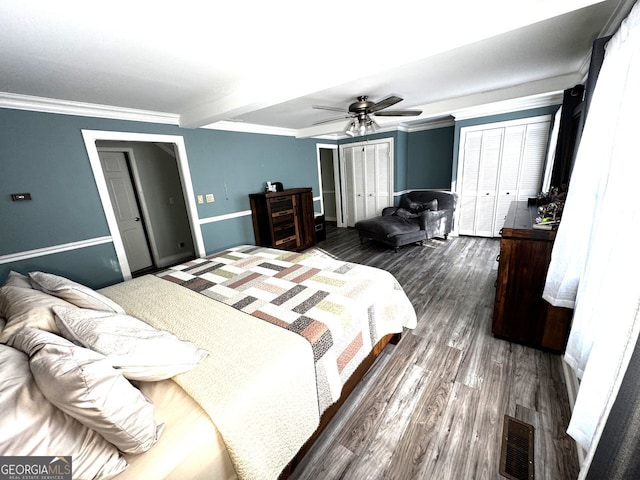 bedroom featuring ornamental molding, dark wood finished floors, visible vents, and multiple closets