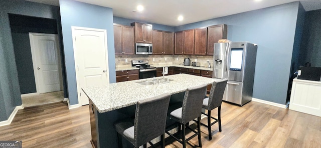 113 Citadel Dr, Hampton, GA 30228 - kitchen featuring appliances with stainless steel finishes, light wood-style flooring, decorative backsplash, a breakfast bar, and a center island with sink