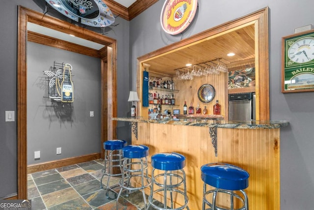 indoor wet bar featuring stone finish flooring, crown molding, and baseboards