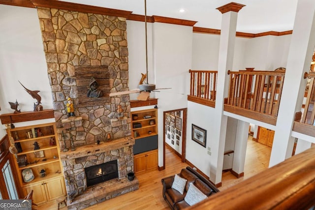 living room featuring a stone fireplace, crown molding, wood finished floors, recessed lighting, and ornate columns