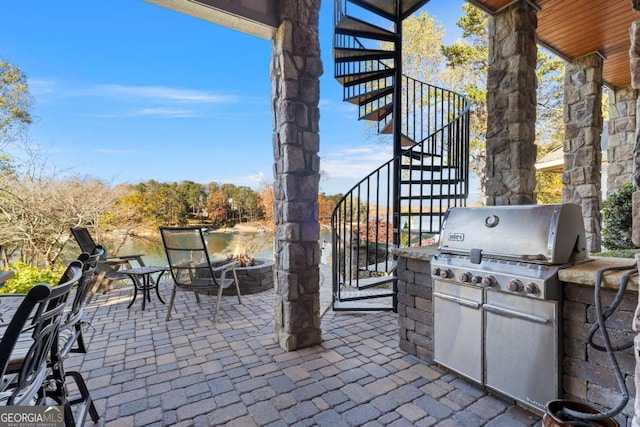 view of patio with stairs, a fire pit, grilling area, and a water view