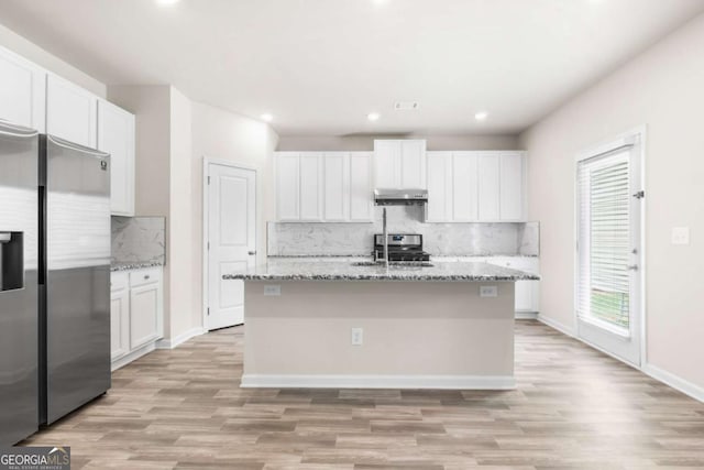 kitchen featuring white cabinets, stainless steel fridge, a kitchen island with sink, and under cabinet range hood