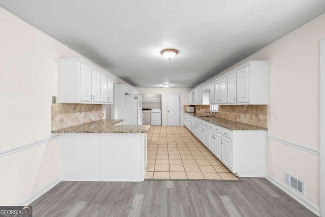 kitchen with separate washer and dryer, white cabinetry, a peninsula, visible vents, and decorative backsplash