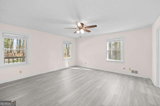 spare room with light wood finished floors, a wealth of natural light, and a ceiling fan