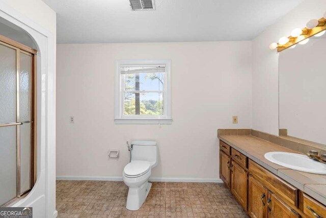 bathroom with toilet, vanity, a shower with door, baseboards, and visible vents