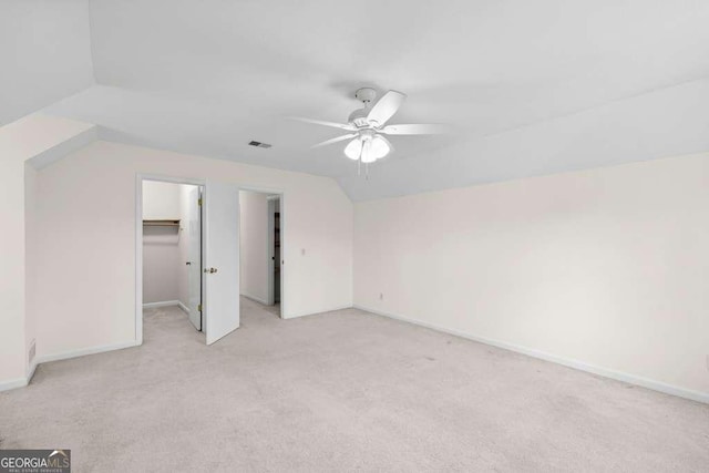 unfurnished bedroom with a walk in closet, vaulted ceiling, baseboards, visible vents, and light carpet