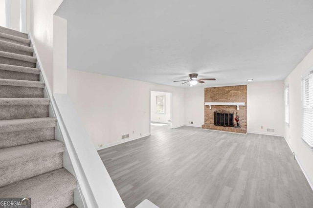 unfurnished living room with wood finished floors, a healthy amount of sunlight, stairs, and ceiling fan