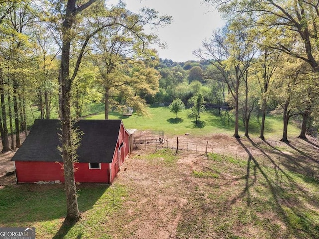 view of yard with fence, a forest view, an outdoor structure, and a barn