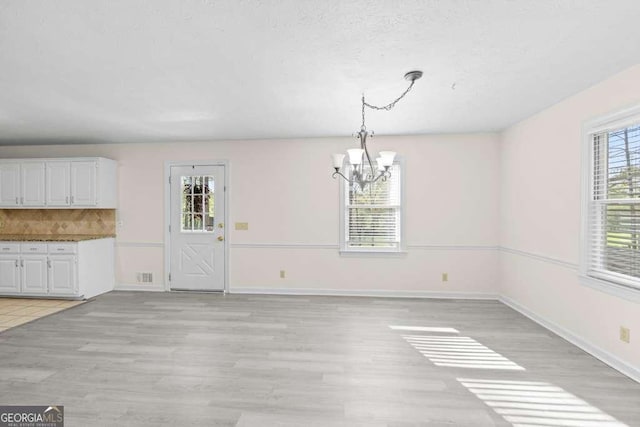 unfurnished dining area with baseboards, a chandelier, and light wood-type flooring