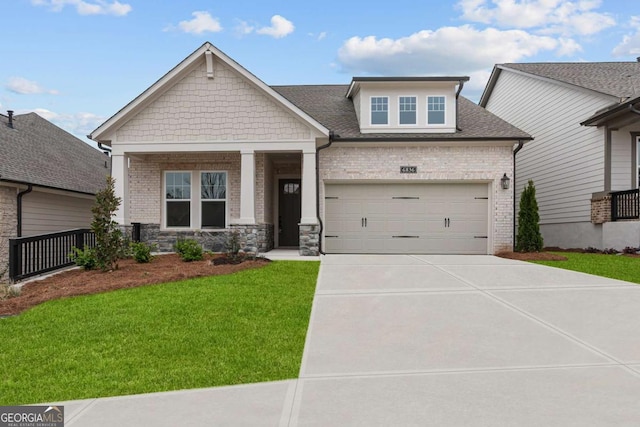 craftsman house featuring a front yard, covered porch, roof with shingles, concrete driveway, and a garage