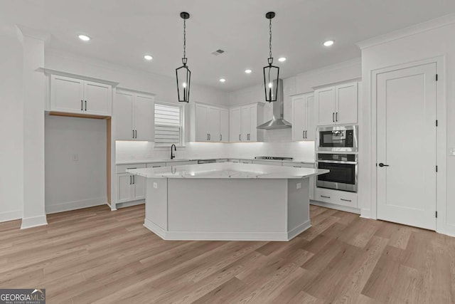 kitchen featuring light wood-style flooring, visible vents, wall chimney exhaust hood, appliances with stainless steel finishes, and a center island