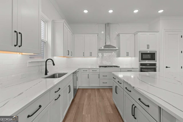 kitchen with a sink, wall chimney exhaust hood, light stone countertops, stainless steel appliances, and white cabinets