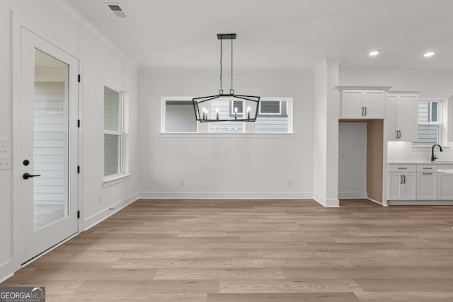 unfurnished dining area featuring light wood-style flooring, visible vents, ornamental molding, a sink, and a notable chandelier