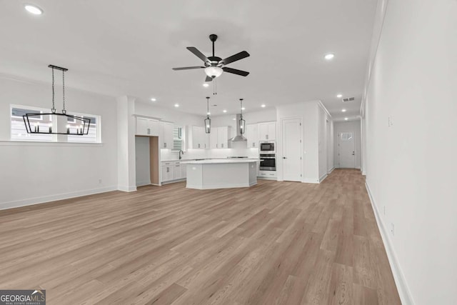unfurnished living room with recessed lighting, ceiling fan with notable chandelier, baseboards, a sink, and light wood-style flooring