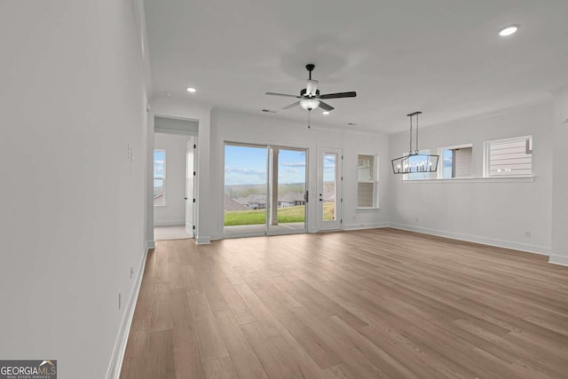 unfurnished living room with recessed lighting, ceiling fan with notable chandelier, and light wood-type flooring