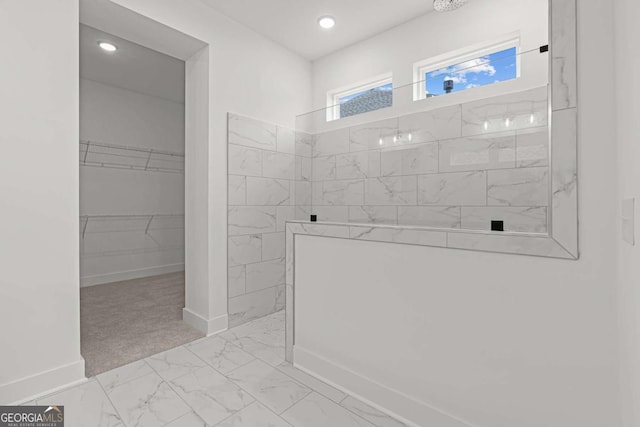 bathroom featuring marble finish floor, baseboards, a spacious closet, and walk in shower