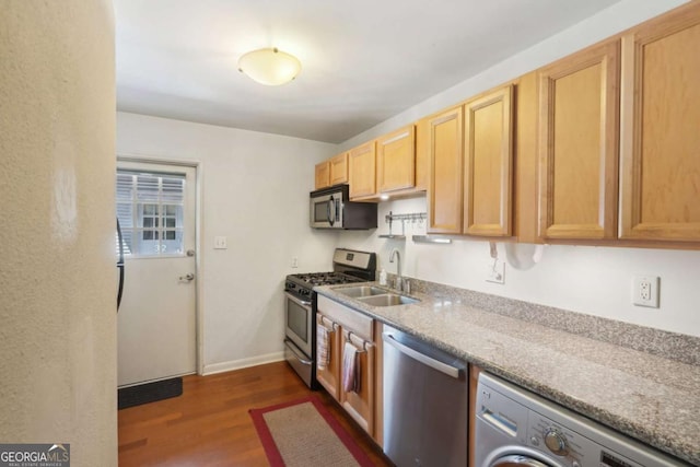 kitchen with dark wood finished floors, a sink, washer / dryer, stainless steel appliances, and baseboards
