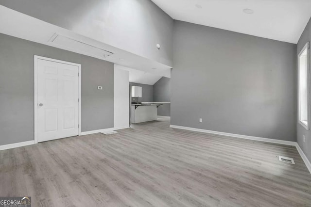 unfurnished living room with attic access, baseboards, lofted ceiling, and wood finished floors
