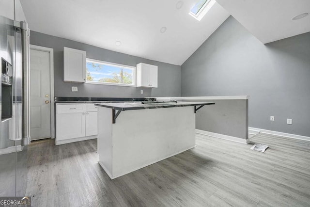 kitchen featuring white cabinets, vaulted ceiling with skylight, a kitchen island, light wood-style floors, and a kitchen breakfast bar