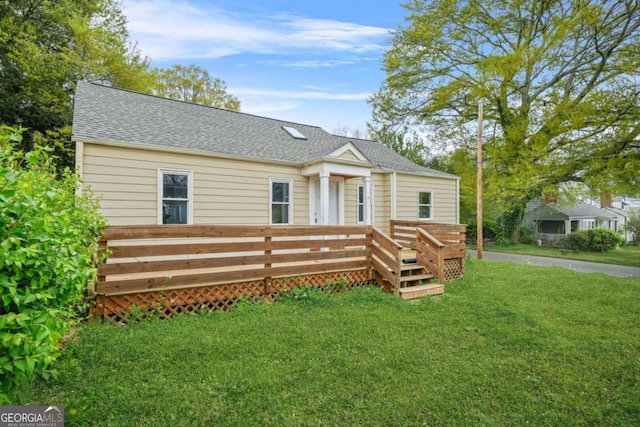 view of front of home with a wooden deck, roof with shingles, and a front yard