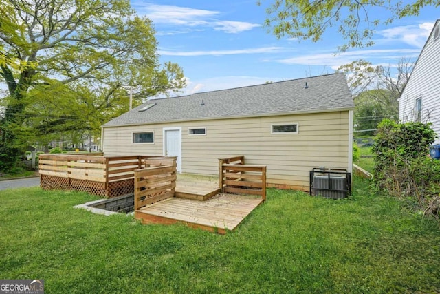 rear view of house with central air condition unit, a wooden deck, roof with shingles, and a yard