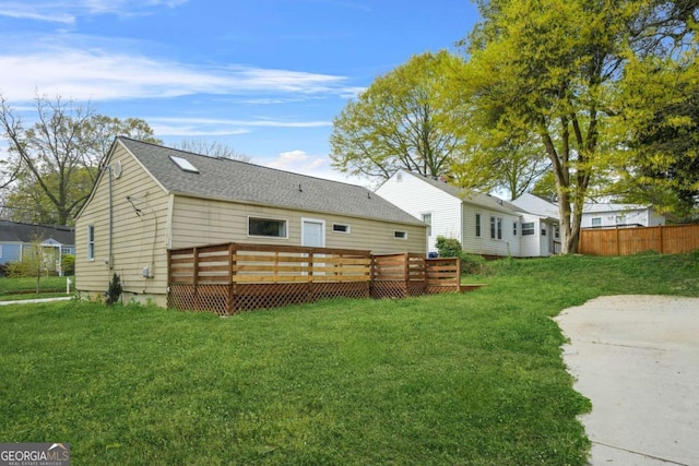 back of property featuring a wooden deck, a shingled roof, and a lawn